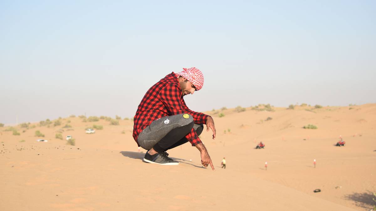Beginner receiving Sandboarding Lessons on a desert dune with instructor nearby